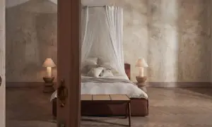 Przytulna sypialnia w stylu boho z baldachimem nad łóżkiem, kamiennymi lampkami i drewnianą podłogą.