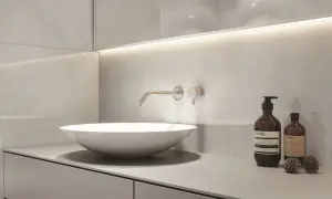 Nowoczesny blat do łazienki z umywalką nablatową i baterią ścienną. Minimalistyczny design, szare płytki i dyskretne oświetlenie.