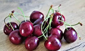 Kupa soczystych, ciemnoczerwonych czereśni, w tym wczesne odmiany, z zielonymi ogonkami, leży na drewnianym blacie.