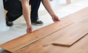 Układanie paneli podłogowych bez wylewki. Ręce mężczyzny precyzyjnie dopasowują kolejny panel do już ułożonej podłogi.