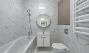 Nowoczesna łazienka z wanną, umywalką i podwieszanym WC. Płytki imitujące marmur dodają elegancji.