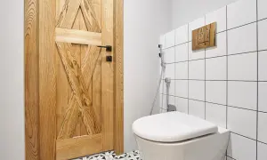 Nowoczesna łazienka z podwieszanym WC, gdzie montaż geberitu w ścianie murowanej jest dyskretnie ukryty za płytkami. Drewniane detale i wzorzysta podłoga dodają ciepła.
