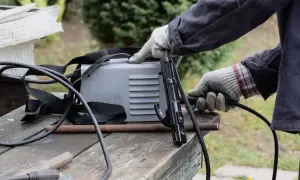 Ręce w rękawiczkach przygotowują spawarkę do domu. Widać uchwyt elektrody i kable.