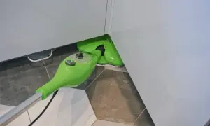 Zielony mop parowy w rogu pomieszczenia, gotowy do sprzątania. Doskonałe zastosowanie do czyszczenia fug i trudno dostępnych miejsc.