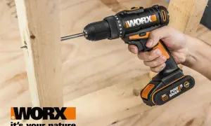 Ręka trzyma wkrętarkę Worx, wiercąc w drewnie. Worx to marka narzędzi dla majsterkowiczów.