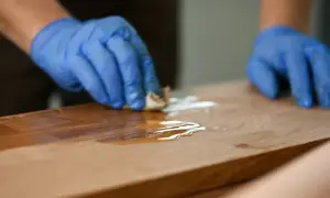 Ręce w niebieskich rękawiczkach nakładają olej na drewniany blat, pokazując, jak odnowić blat kuchenny laminowany.