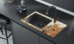 Elegancka budowa zlewu kuchennego z czarną komorą i ozdobnym, złotym wzorem na rancie. Nowoczesny kran i akcesoria dopełniają całość.