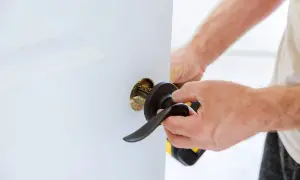 Mężczyzna dokonuje wymiany klamki w drzwiach wejściowych, używając wkrętarki.