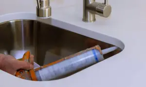 Uszczelnianie otworu pod umywalkę nablatową. Pistolet z silikonem w ręce.