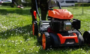 Pomarańczowa kosiarka spalinowa gotowa do pracy. Widać jej moc i solidną konstrukcję, która poradzi sobie z każdym trawnikiem.