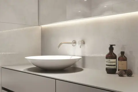 Nowoczesny blat do łazienki z umywalką nablatową i baterią ścienną. Minimalistyczny design, szare płytki i dyskretne oświetlenie.