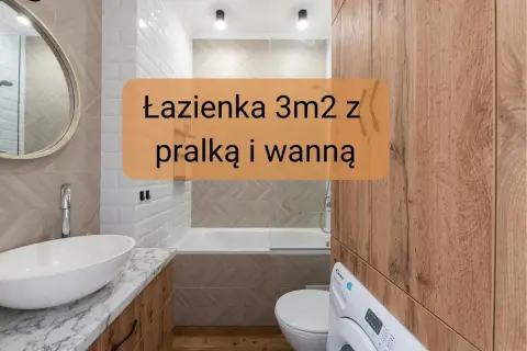 Kompaktowa łazienka z wanną i pralką. Białe płytki, drewniane akcenty i okrągłe lustro tworzą przytulną przestrzeń.