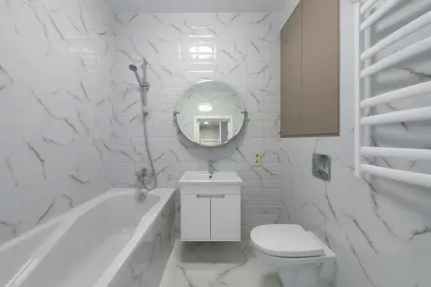 Nowoczesna łazienka z wanną, umywalką i podwieszanym WC. Płytki imitujące marmur dodają elegancji.