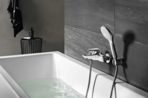Elegancka bateria prysznicowa zamontowana na ścianie nad wanną, z której leje się woda.