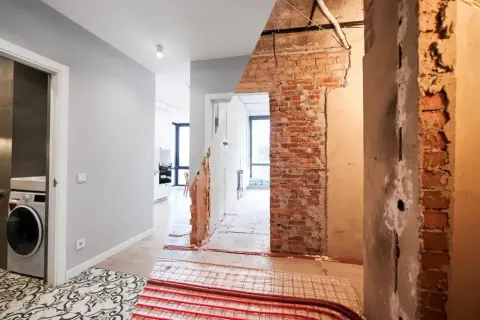 Przed i po remoncie starego domu. Widok na korytarz z pralką i łazienką po lewej, oraz odsłoniętą ceglaną ścianę i instalacje po prawej.