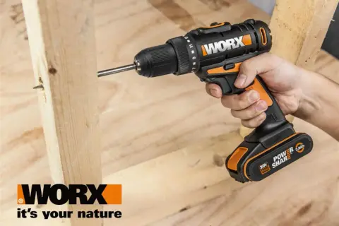 Ręka trzyma wkrętarkę Worx, wiercąc w drewnie. Worx to marka narzędzi dla majsterkowiczów.