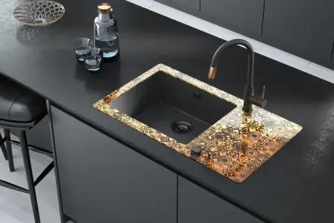 Elegancka budowa zlewu kuchennego z czarną komorą i ozdobnym, złotym wzorem na rancie. Nowoczesny kran i akcesoria dopełniają całość.