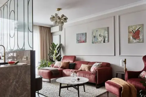 Elegancka ściana w salonie z sofą w kolorze cegły, obrazami i designerską lampą.