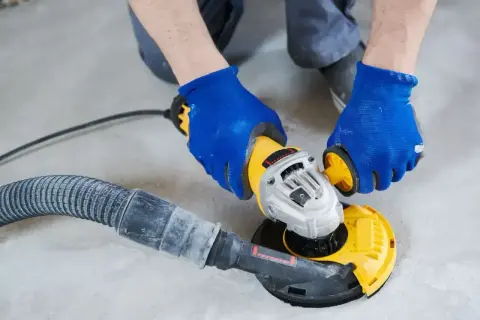 Ręce w niebieskich rękawiczkach wykonują polerowanie szlifierką kątową z odsysaniem pyłu.