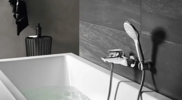 Elegancka bateria prysznicowa zamontowana na ścianie nad wanną, z której leje się woda.