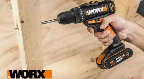 Ręka trzyma wkrętarkę Worx, wiercąc w drewnie. Worx to marka narzędzi dla majsterkowiczów.