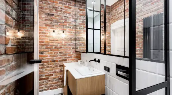 Nowoczesna łazienka w stylu loft z ceglaną ścianą, drewnianą szafką pod umywalkę i czarnymi metalowymi elementami.