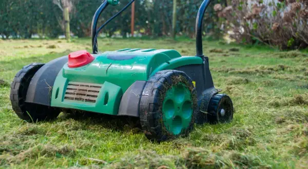 Zielony aerator na trawniku, gotowy do pracy. Zastanawiasz się, aerator co to? To urządzenie do napowietrzania gleby.