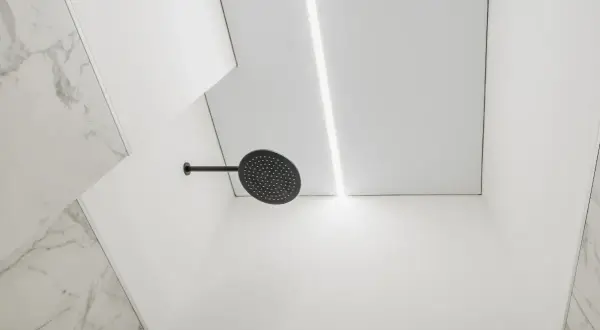 Nowoczesny sufit podwieszany w łazience z ukrytym oświetleniem i czarną deszczownicą.
