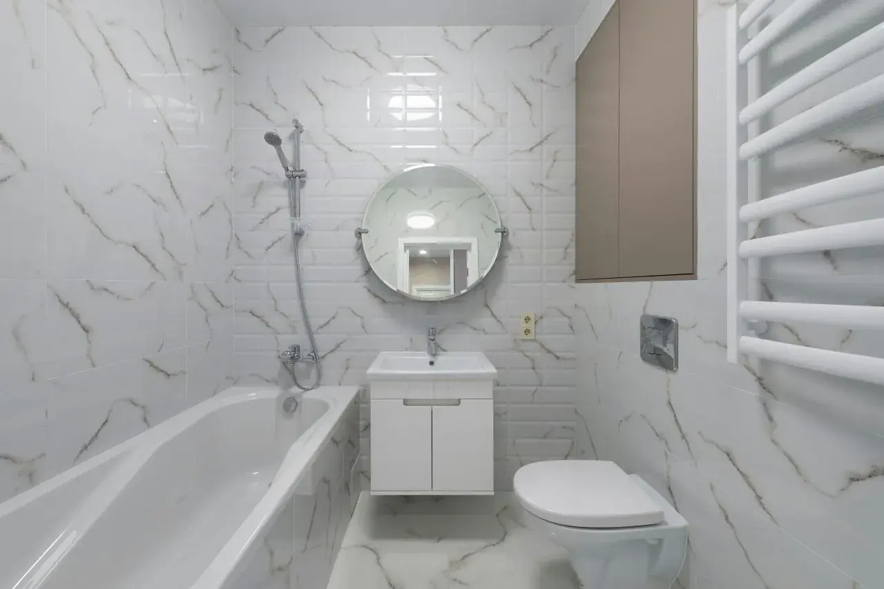 Nowoczesna łazienka z wanną, umywalką i podwieszanym WC. Płytki imitujące marmur dodają elegancji.