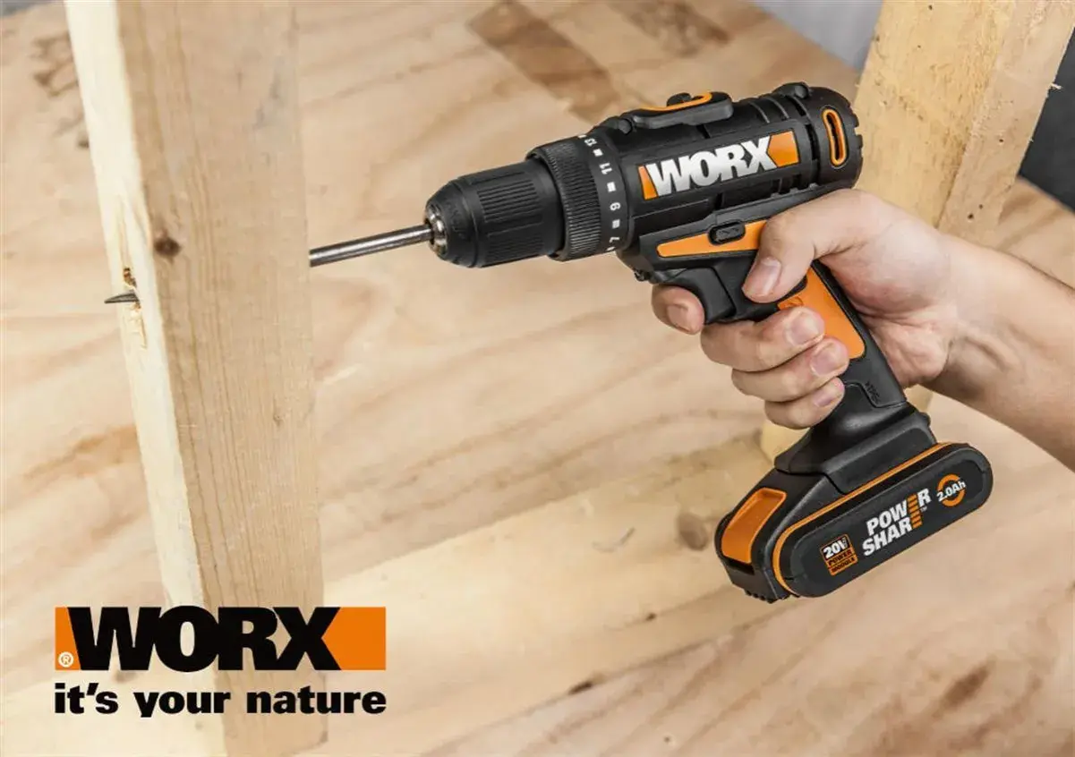 Ręka trzyma wkrętarkę Worx, wiercąc w drewnie. Worx to marka narzędzi dla majsterkowiczów.