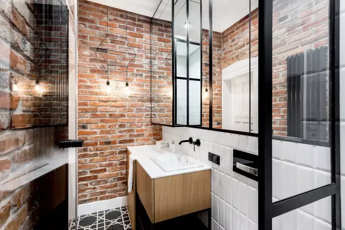 Nowoczesna łazienka w stylu loft z ceglaną ścianą, drewnianą szafką pod umywalkę i czarnymi metalowymi elementami.