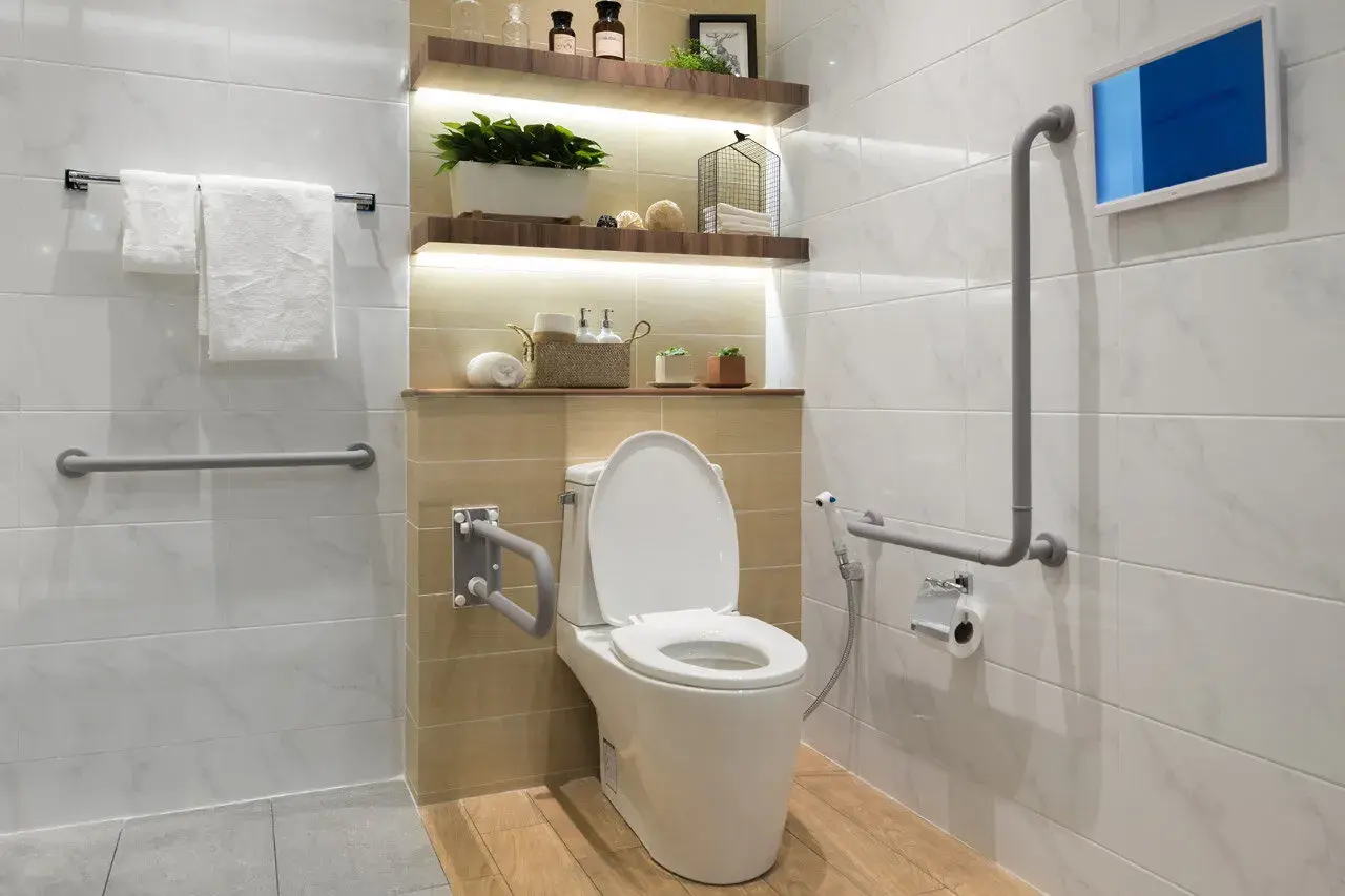 Nowoczesna łazienka dla niepełnosprawnych z uchwytami, podwieszanym sedesem i ekranem.