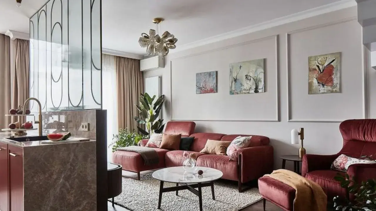 Elegancka ściana w salonie z sofą w kolorze cegły, obrazami i designerską lampą.
