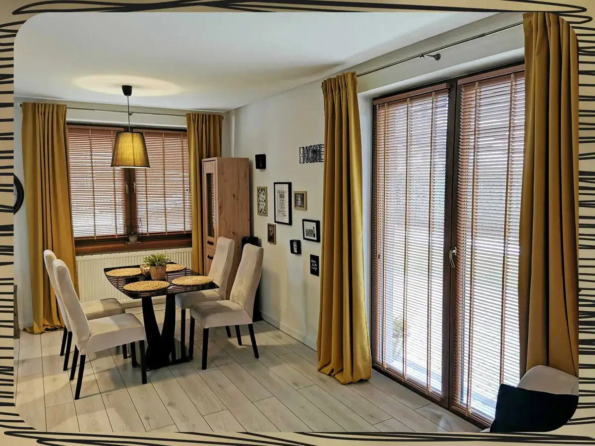 Elegancki salon z jadalnią, gdzie złote zasłony i mechanizm żaluzji drewnianych tworzą przytulną atmosferę.