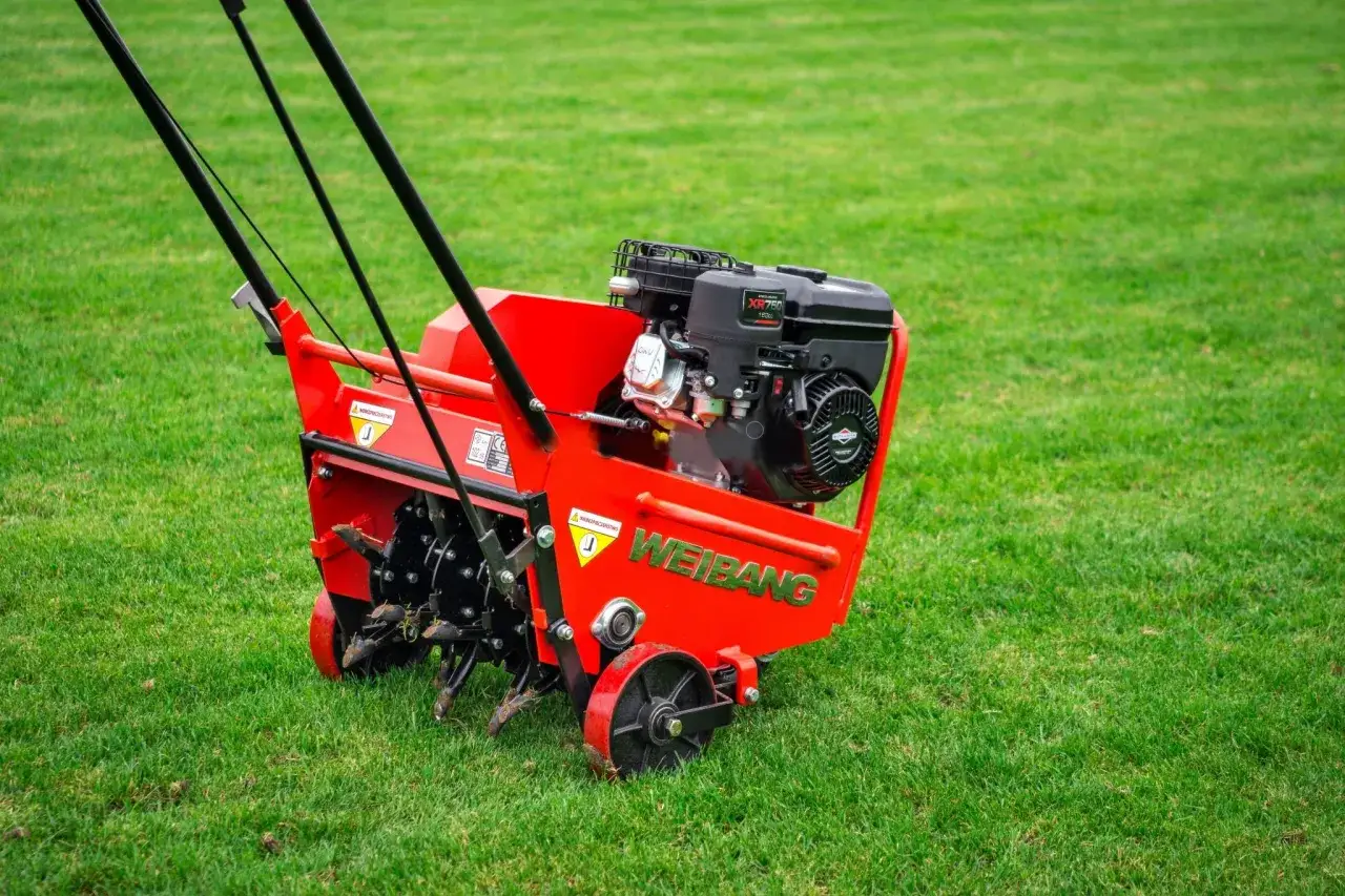 Czerwony aerator Weidemann na zielonej trawie. Idealny sprzęt, gdy robić aerację trawnika, by zapewnić mu lepsze dotlenienie i wzrost.