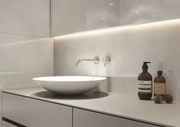 Nowoczesny blat do łazienki z umywalką nablatową i baterią ścienną. Minimalistyczny design, szare płytki i dyskretne oświetlenie.