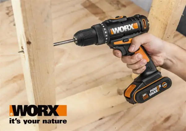 Ręka trzyma wkrętarkę Worx, wiercąc w drewnie. Worx to marka narzędzi dla majsterkowiczów.