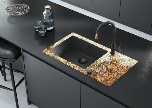 Elegancka budowa zlewu kuchennego z czarną komorą i ozdobnym, złotym wzorem na rancie. Nowoczesny kran i akcesoria dopełniają całość.